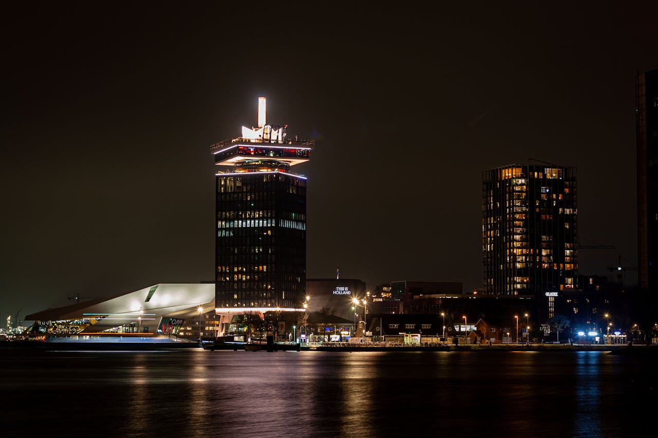 Night view of A'DAM Tower and Amsterdam skyline reflected in the water.