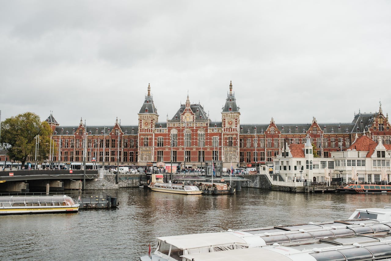 Iconic view of Amsterdam Centraal Station with boats on the river, showcasing urban architecture.